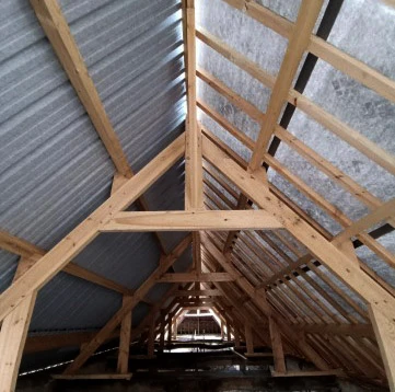Intérieur d'une charpente en bois traditionnelle avec poutres apparentes et fermes triangulaires