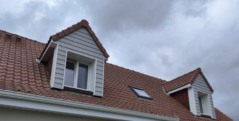 Façade de maison résidentielle avec toiture en tuiles terre cuite et lucarnes à bardage blanc