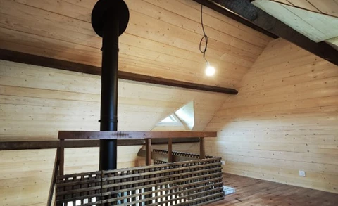 Intérieur d'un chalet en bois avec mezzanine, poutre apparente et conduit de poêle noir