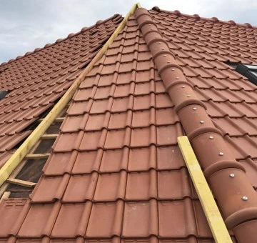 Chantier de couverture en cours, vue extérieure d'une toiture en pente avec ouvrier installant des tuiles terre cuite