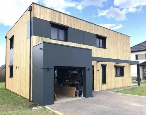 Maison moderne à deux niveaux avec façade mixte bois et métal gris anthracite, garage ouvert au rez-de-chaussée, terrain résidentiel avec pelouse